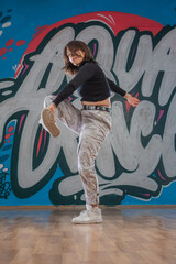 Fototapeta na wymiar Attractive young woman doing breakdance move over graffiti background