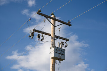 A wooden power pole and transformer with communication and transmission lines under a blue sky background. - obrazy, fototapety, plakaty