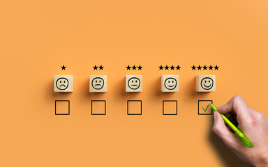hand selecting a happy emoticon symbolizing a very good review on orange background - 434215215