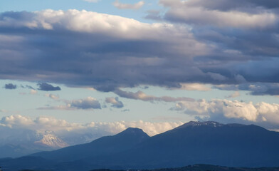 Fototapeta na wymiar Grandi nuvole sopra le montagne dell’Appennino all’imbrunire in un cielo azzurro primaverile