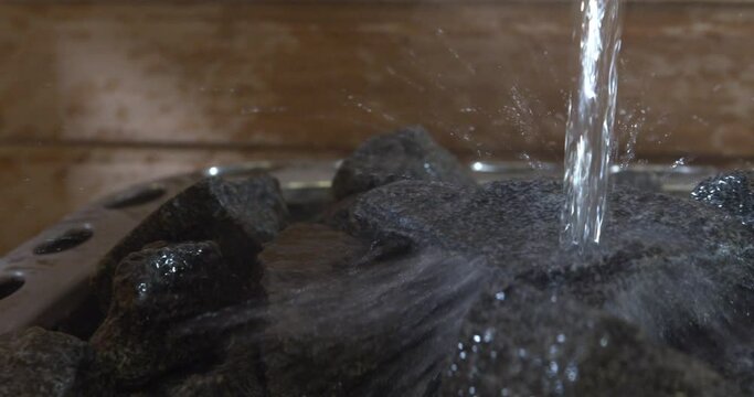 Pouring water on hot sauna rocks to generate steam inside the sauna