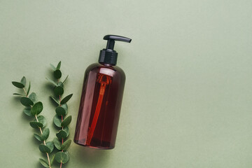 Dark dispenser bottle of shower gel or soap, and eucalyptus branches on a green background. SPA...