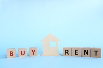 Buying versus renting house concept. Wooden house model with buy or rent word on wooden blocks.