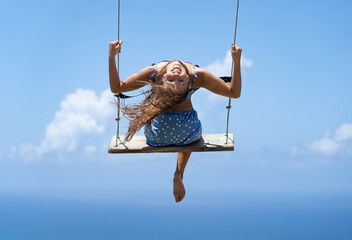 Young beautiful caucasian woman on the rope swing with sea and sky background. Concept of freedom and happiness 