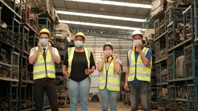 Various Races Workers: Asians, Blacks, And Caucasians In Factory Safety Uniforms And Helmets Wearing Masks At The Same Times In Warehouse To Prevent Coronavirus (COVID 19).