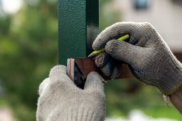 close-up of a male joiner measuring the incision with a ruler and pencil on the grass in the village