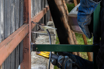 Close up of the a welder welds a fence on the construction site in the village. Construction on a metal frame.