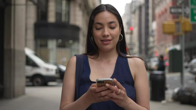 Young Latina Hispanic woman in city walking street texting on cellphone