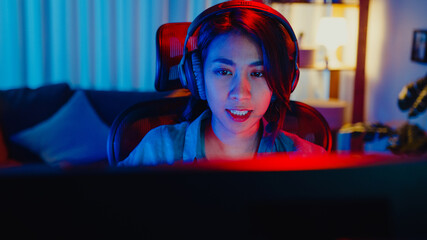 Close-up face happy asia professional girl gamer wear headphone competition play video game neon light computer in living room at home. Esport streaming game online, Home quarantine activity concept.