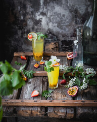 berry and passionfruit cocktails in glasses on wooden table with seasonal flowers and fresh fruit, refreshing drink concept