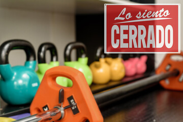 in Spanish inscription sorry we are closed. compliance with sanitary measures during a pandemic. Set of colorful iron modern kettlebbells on rack in gym