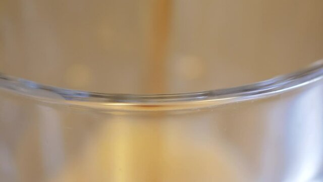 The lip of a large glass in focus as a dark fizzy diet soda is being poured to the the top. The high concentration of carbonation in the drink is clearly visible as tiny bubbles jumps on the surface.
