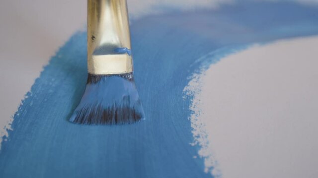 CLOSE UP, DOF: Unrecognizable artist drags their paintbrush across a blank slate of paper while creating their newest masterpiece. Painter uses a fine paintbrush to paint a blue line with oil paint.