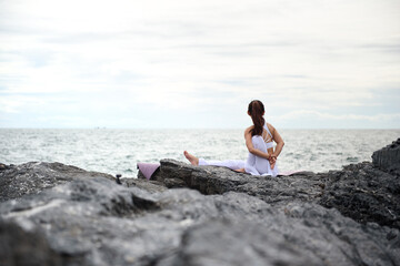 Asian young woman practicing yoga in exercise while looking out to the sea. Stretching &...