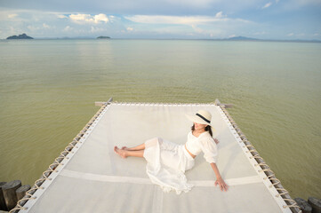 Obraz premium A happy beautiful woman in white dress enjoying and relaxing on terrace at the tropical island and turquoise clear ocean, Summer and holidays concept