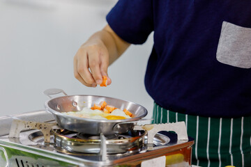Smart kid on black shirt of modern family carefully pouring ingredients into flying pan for cooking easy breakfast as learning from mom in home kitchen