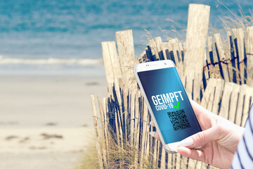 Strand, eine Frau mit Smartphone und elektronischer Impfpass Covid-19