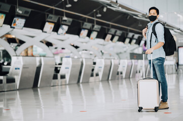Asian man traveler wearing mask for protect from coronavirus standing with luggage 