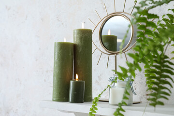 Burning candles, mirror and houseplant on shelf near light wall