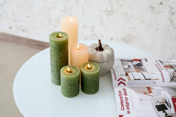 Burning candles and magazine on table in room, closeup