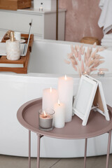 Burning candles and blank frame on table in bathroom