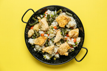 Frying pan with cooked vegetables, chicken and rice on color background