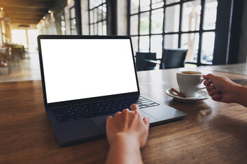 Fototapeta premium Mockup image of a woman using and touching on laptop touchpad with blank white desktop screen while drinking coffee