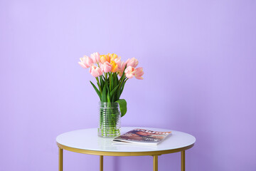 Bouquet of tulip flowers and magazine on table near color wall