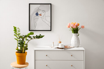 Tulip flowers on chest of drawers near white wall
