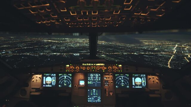 Airplane flying over city at night for landing. Able to see beautiful view and city lights. View from inside cockpit. Pilot eye view.