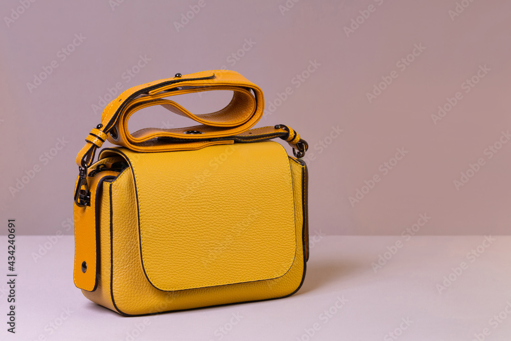 Canvas Prints Bright yellow leather women's handbag on beige fabric background. Fashion and shopping concept