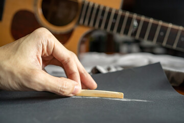 Fototapeta na wymiar Lower the height of an acoustic guitar saddle for a better playability by sanding down a bone saddle with sandpaper