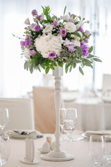 Centerpiece made of green leaves and fresh flowers stands on the dinner table. Wedding day. Fresh flowers decorations.