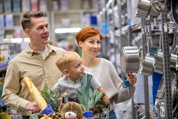 Friendly family choosing dishes, pans and pots, making purchase. kitchen utensils for customers in supermarket, shopping together concept, redhead woman make choice, examining assortment