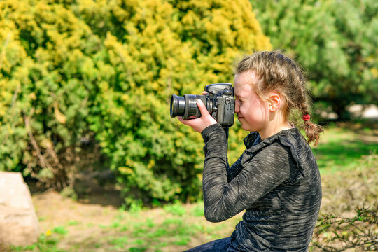 A young girl photographs nature in the park with a SLR camera.