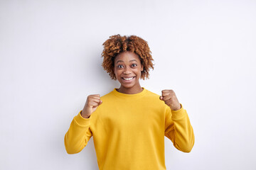 excited african lady raising hands up, cheering, happily smiling, celebrating victory, dressed casually, isolated on white studio background