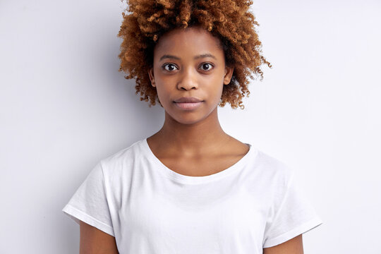 Confident calm afro woman with curly short hair look at camera, wearing white t-shirt, posing looking serious. portrait