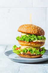 Vegan burger with vegetables and hummus, gray background. Plant-based diet concept.