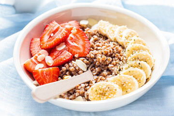 Close up of buckwheat porridge with banana and berries in white bowl. Healthy breakfast concept.