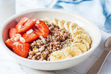 Close up of buckwheat porridge with banana and strawberry in white bowl. Healthy breakfast concept.