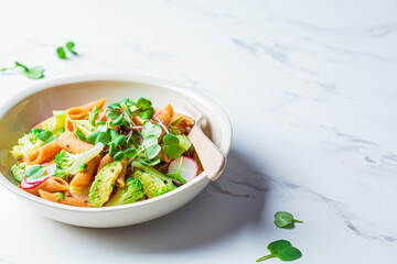 Lentil pasta with broccoli, avocado, radish and sprouts in white bowl. Healthy vegan recipe concept.
