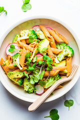 Lentil pasta with broccoli, avocado, radish and sprouts in white bowl, top view. Healthy vegan recipe concept.