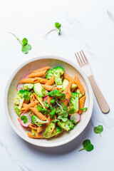 Lentil pasta with broccoli, avocado, radish and sprouts in white bowl, top view. Healthy vegan recipe concept.