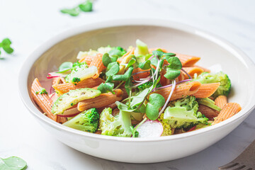 Lentil pasta with broccoli, avocado, radish and sprouts in white bowl. Healthy vegan recipe concept.