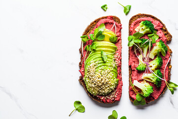 Toasts with beetroot hummus, avocado and broccoli, white marble background. Vegan food concept.
