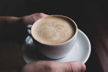 White cappuccino cup in the hands of a man