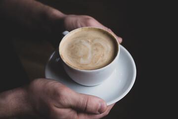 White cappuccino cup in the hands of a man