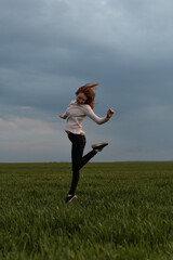 Portrait of cheerful positive girl jumping in the field against stormy sky