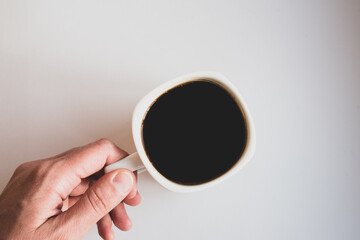 Hand holding a white mug with black coffee on a white background