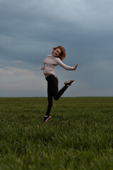 Fototapeta na wymiar Portrait of cheerful positive girl jumping in the field against stormy sky